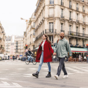 A smiling couple holding hands as they cross the road in Paris.