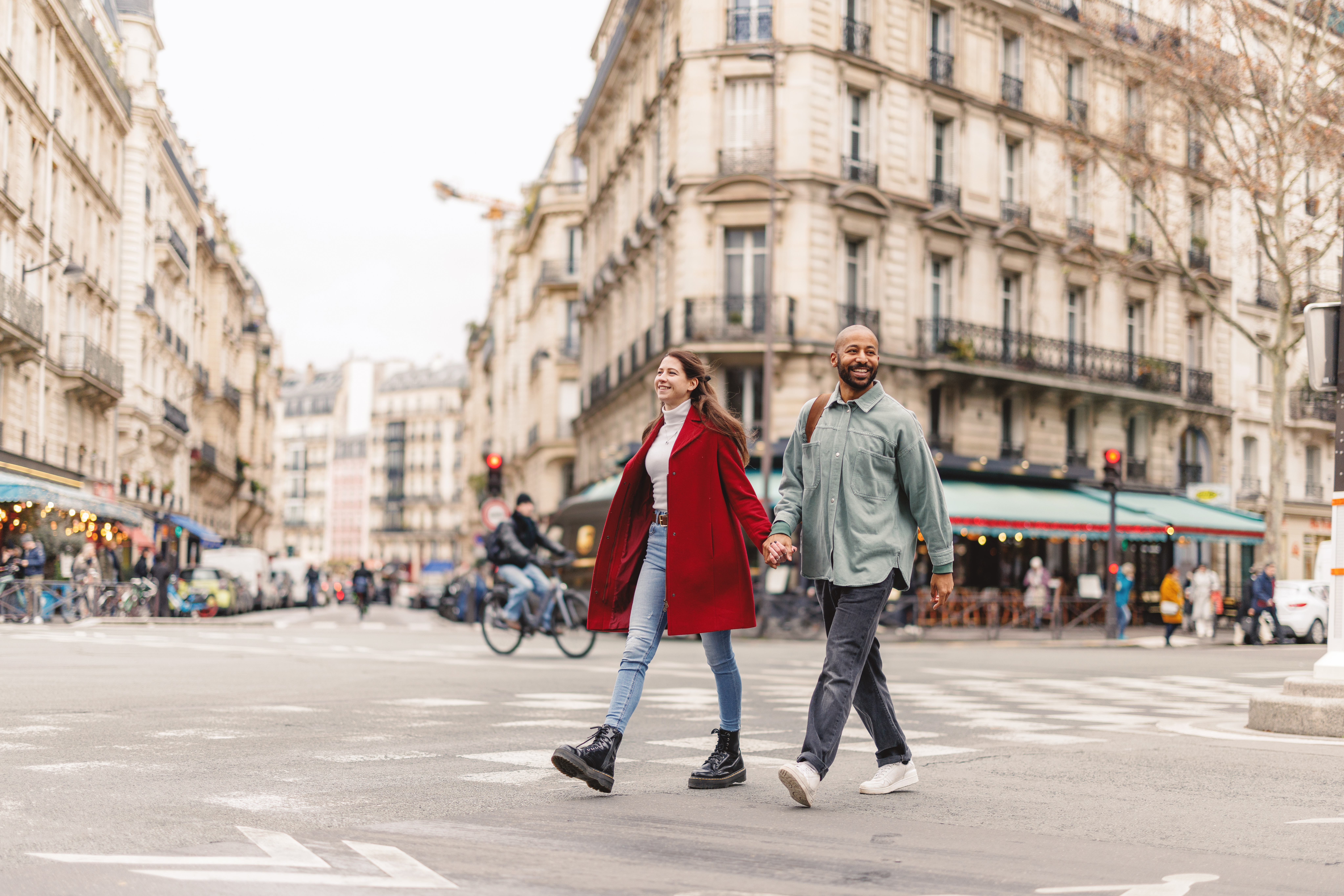 A smiling couple holding hands as they cross the road in Paris.